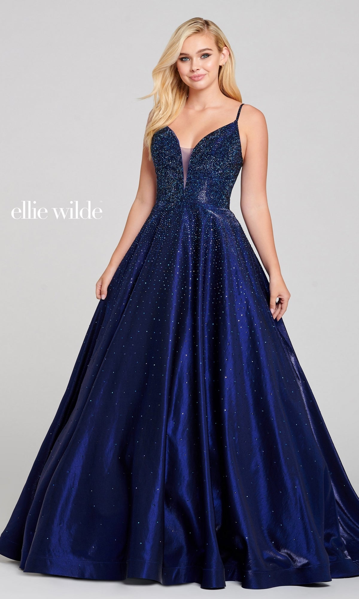 A woman wearing the Ellie Wilde EW121005 long beaded prom ball gown, featuring a deep blue hue, floor-length design, open back, fitted bodice, and subtle sparkling embellishments.